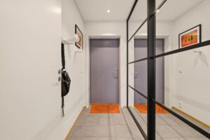 Lysmalt og flott gang med fliser på gulvet, innfelte downlights i himlingen og skyvedørsgarderobe med speilglass og sorte detaljer.