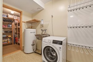 Praktisk vaskerom med utslagsvask, varmtvannstank og opplegg for vaskemaskin. Rommet har oppgraderingsbehov. Inngang til bod for gode lagringsmuligheter. 