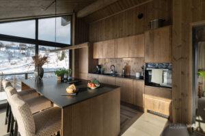 Åpent kjøkken med god arbeidsplass – perfekt for lange, gode kvelder på fjellet. er kombineres funksjonalitet og hyttekos i ekte høyfjellsstil. Skaplass begge sider av øyen, platetopp med ventilator og spesialbygd lampe over kjøkkenøy fra Fjellmøbler AS.