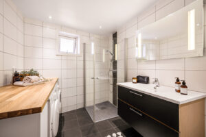Badet inneholder møblement/speil og belysning, vegghengt toalett, innfelbart dusjhjørne i glass, dusjgarnityr, opplegg for
vaskemaskin/tørketrommel, innredning/skap og benkeplate
