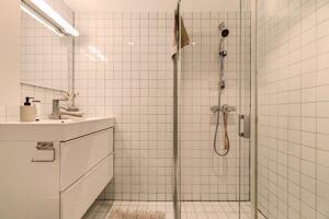 Tidløst, flislagt bad fra byggeår med varmekabler i gulv. I tillegg praktisk innredning med servant, speil og høyskap