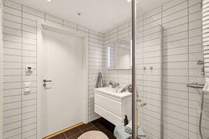 Badet har vegghengt toalett, servantinnredning og dusj med glassdører.