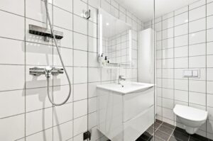 Badet har blant annet flislagte gulv og vegger, behagelig gulvvarme, innfelte downlights i himlingen, vegghengt toalett med innebygget sisterne og dusjsone med glassvegg.
